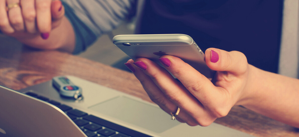 A woman's hands, at desk with laptop computer, Apple iPhone smartphone in her hand, phoning us using the phone number from the Contact Us information on our Web site