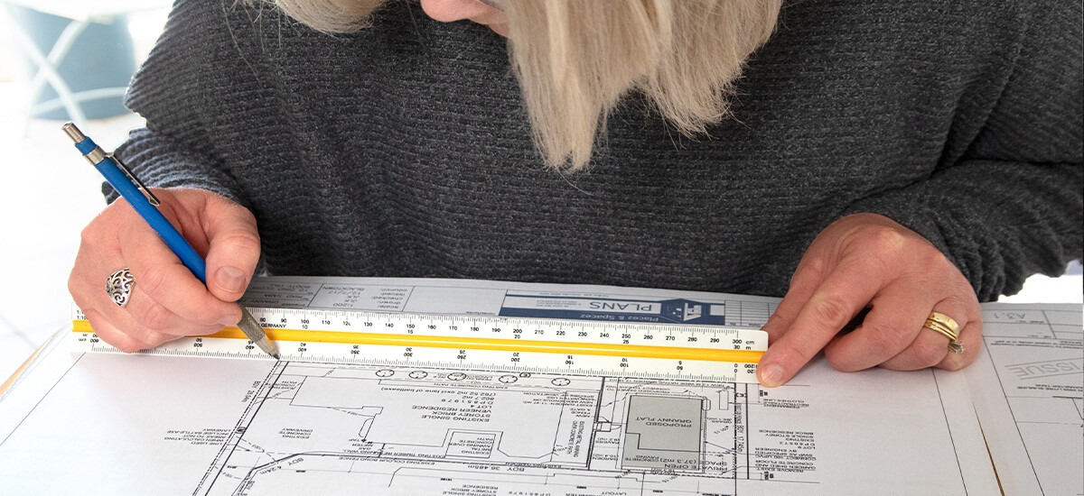 Carefully Checking Architectural Site Plan in Office. The Civil Designer and draftsman, pencil and scale rule in hands, carefully checking and marking up architectural site plan in office