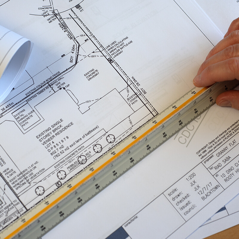 Careful checking of architectural site plan. Scale rule in hands, civil draftsman carefully checking and marking up architectural site plan in office