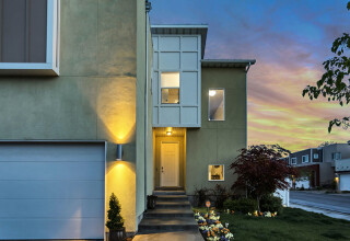 Two story house with external and internal lighting illuminated to accentuate colours of garden flowers during evening sky at sunset