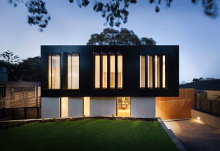 Contemporary two-storey house with vertical windows and lighting at sunset