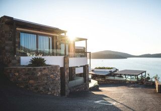 Modern two-storey house on sloping land, lake or ocean inlet water views behind at sunset